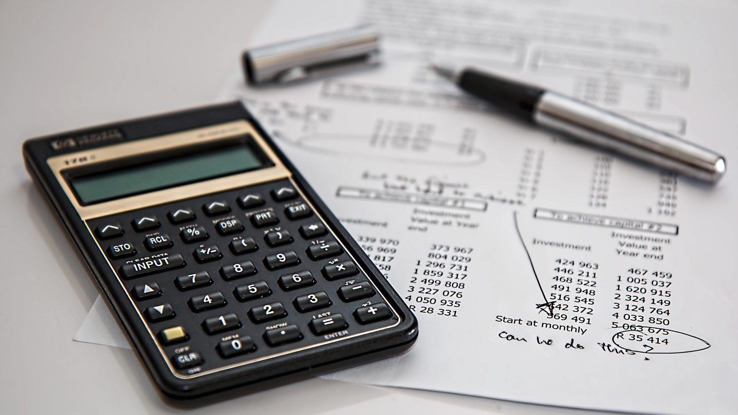 Calculadora e caneta sobre um relatório financeiro impresso com anotações